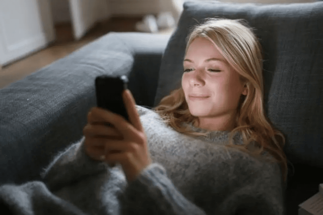Frau entspannt mit dem Smartphone auf dem Sofa